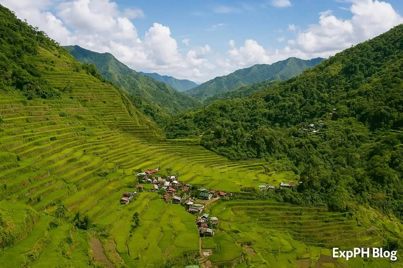 Realistic view of the Banaue Rice Terraces in Ifugao with layered green fields, mountain landscape, village homes, blue sky, and the ExpPH Blog logo at the bottom corner.