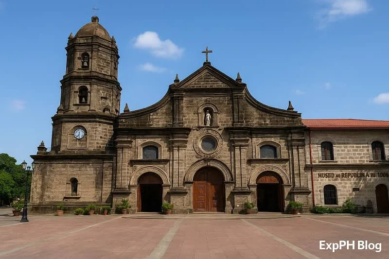Realistic view of Barasoain Church in Bulacan with its stone facade, bell tower, open courtyard, clear blue sky, and the ExpPH Blog logo in the lower corner.