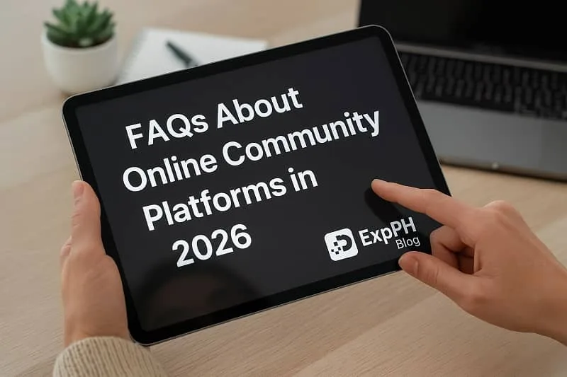 A realistic close up photo of a person holding a tablet displaying the text FAQs About Online Community Platforms in 2026, with the ExpPH Blog logo at the bottom, placed on a wooden desk with a laptop, notebook, and plant in the background.
